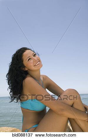 Stock Photo - Hispanic woman sitting on beach. Fotosearch