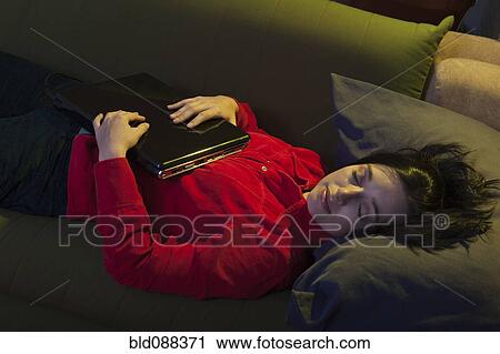 Stock Image - Hispanic woman sleeping on sofa holding laptop. Fotosearch
