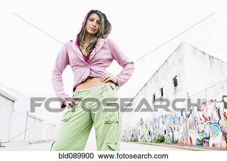Stock Image - Hispanic woman standing in urban alley. Fotosearch
