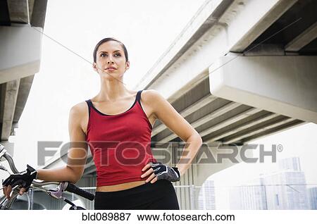 Stock Photo - Hispanic woman standing in urban area with bicycle. Fotosearch