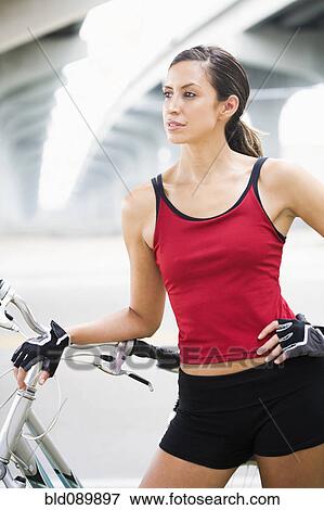 Stock Photo - Hispanic woman standing with bicycle in urban area. Fotosearch