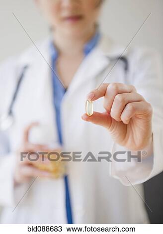 Stock Image - Korean doctor holding out capsule. Fotosearch