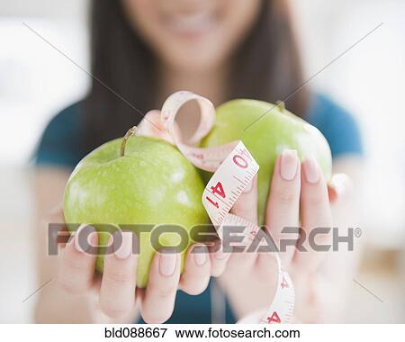 Stock Photo - Korean woman holding apples and tape measure. Fotosearch