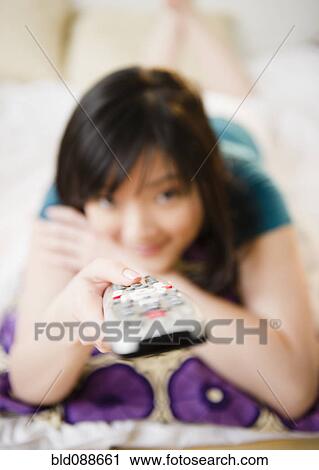 Stock Image - Korean woman holding remote control. Fotosearch