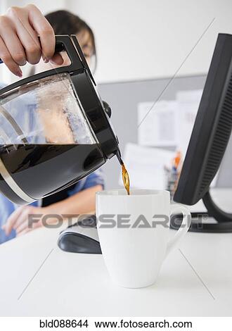 Picture - Korean woman pouring coffee at desk. Fotosearch
