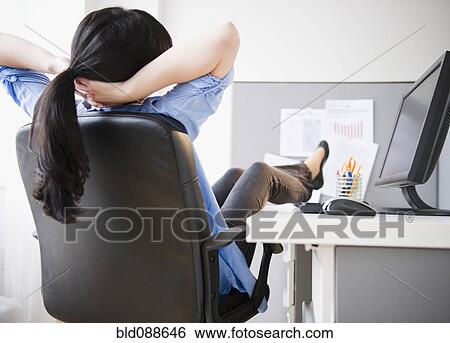 Stock Photograph - Korean woman sitting at desk with feet up. Fotosearch