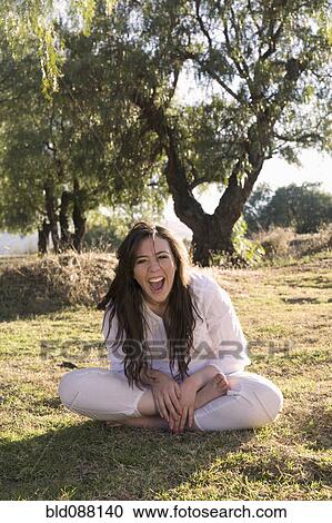 Stock Image - Laughing Hispanic woman sitting in grass. Fotosearch