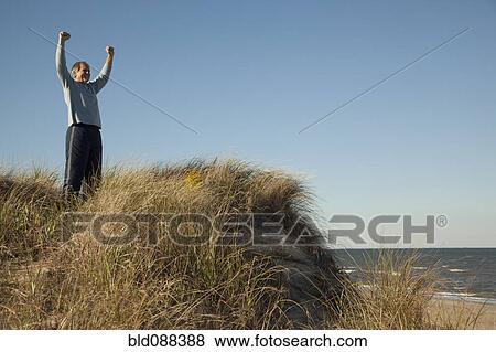 Stock Photo - Man cheering on sand dune near ocean. Fotosearch