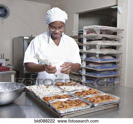 Stock Image - Mixed race baker icing pastry in commercial kitchen. Fotosearch