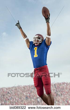 Stock Image - Mixed race football player with arms raised holding football. Fotosearch