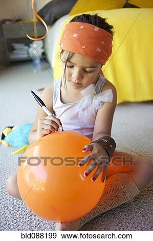Stock Photo - Mixed race girl drawing on balloon. Fotosearch