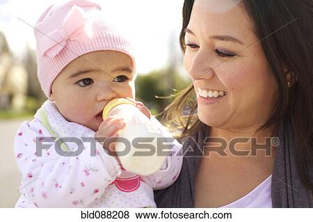 Stock Photo - Mixed race mother watching baby girl drinking bottle. Fotosearch