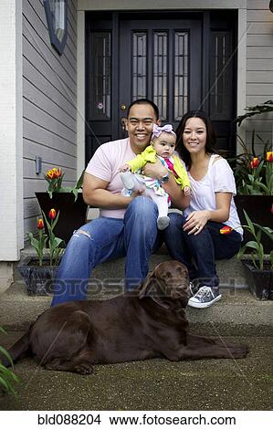 Picture - Mother and father sitting on front stoop with baby girl and dog. Fotosearch