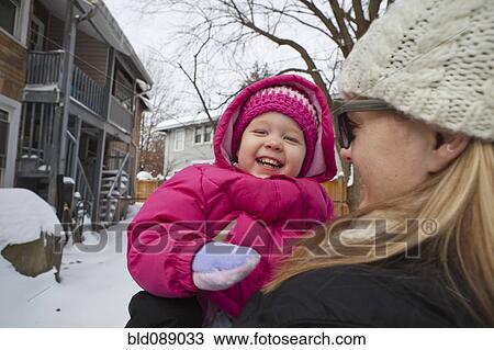 Stock Image - Mother holding grinning girl in coat. Fotosearch