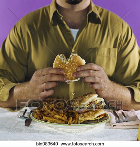 Stock Image - Overweight man eating hamburgers and french fries. Fotosearch