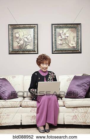 Stock Image - Senior Caucasian woman using laptop on sofa. Fotosearch