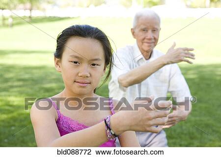 Stock Image - Senior Chinese grandfather and granddaughter doing tai chi outdoors. Fotosearch