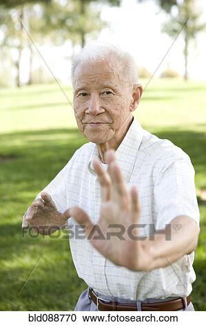 Stock Image - Senior Chinese man doing tai chi outdoors. Fotosearch