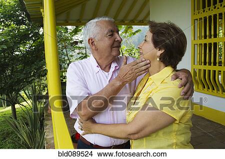 Picture - Senior Hispanic couple hugging on porch. Fotosearch