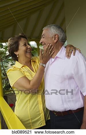 Stock Image - Senior Hispanic couple hugging on porch. Fotosearch