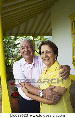 Stock Image - Senior Hispanic couple hugging on porch. Fotosearch