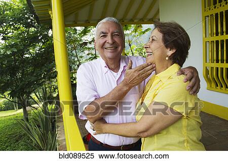 Stock Photography - Senior Hispanic couple hugging on porch. Fotosearch