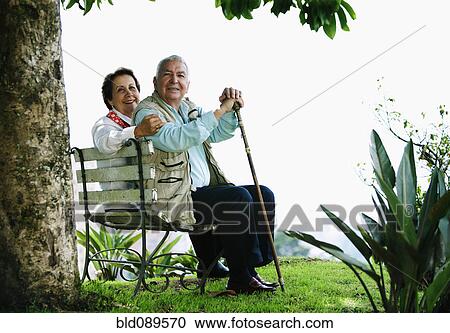Stock Image - Senior Hispanic couple sitting on park bench. Fotosearch