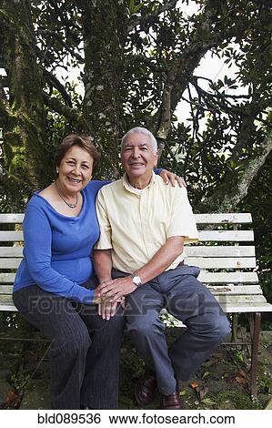 Stock Photograph - Senior Hispanic couple sitting on park bench. Fotosearch