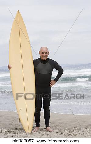 Stock Photo - Senior Hispanic man holding surfboard on beach. Fotosearch