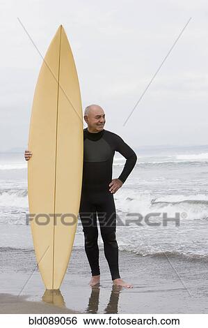 Senior Hispanic man holding surfboard on beach View Large Photo Image Stock Photograph - Senior Hispanic man holding surfboard on beach. Fotosearch