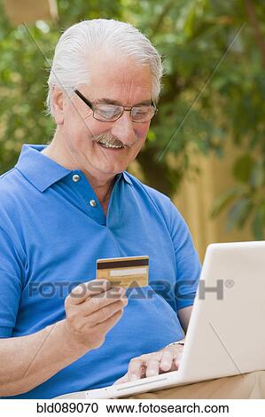 Stock Image - Senior Hispanic man shopping online with credit card. Fotosearch