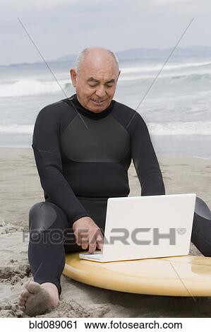 Senior Hispanic man sitting on surfboard using laptop View Large Photo Image Stock Image - Senior Hispanic man sitting on surfboard using laptop. Fotosearch