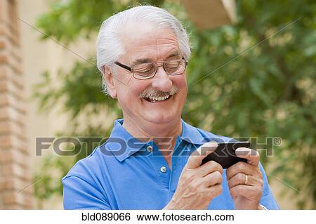 Stock Photograph - Senior Hispanic man text messaging on cell phone. Fotosearch