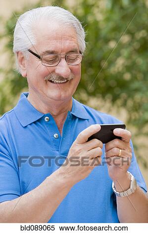 Stock Photography - Senior Hispanic man text messaging on cell phone. Fotosearch