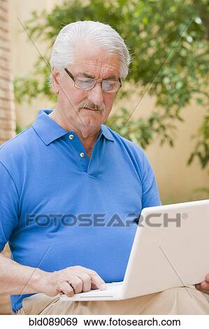 Stock Photo - Senior Hispanic man using laptop outdoors. Fotosearch