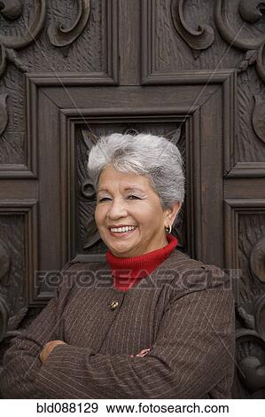 Stock Photo - Senior Hispanic woman leaning against door. Fotosearch