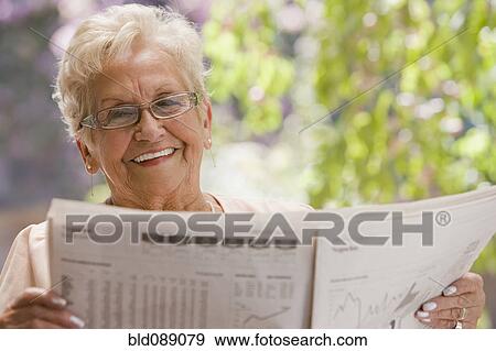 Stock Photo - Senior Hispanic woman reading financial newspaper. Fotosearch