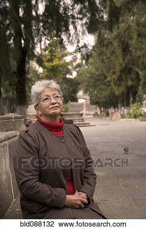 Stock Image - Senior Hispanic woman sitting in park. Fotosearch