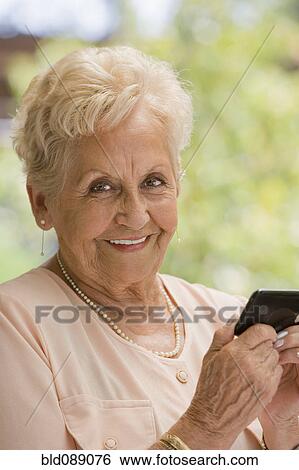 Stock Photograph - Senior Hispanic woman text messaging on cell phone. Fotosearch