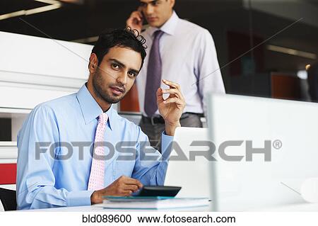 Stock Image - Serious businessman sitting at desk. Fotosearch