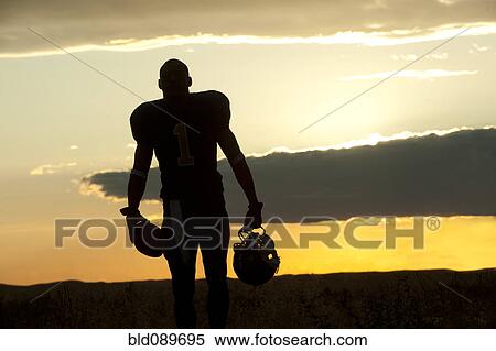 Stock Photography - Silhouette of Black football player carrying helmet and football. Fotosearch