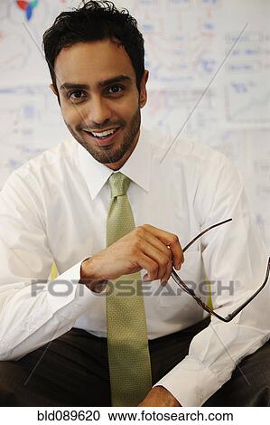 Stock Image - Smiling businessman holding eyeglasses. Fotosearch
