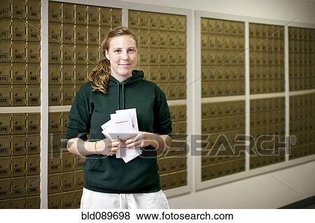 Stock Photo - Smiling Caucasian woman holding letters in mailroom. Fotosearch