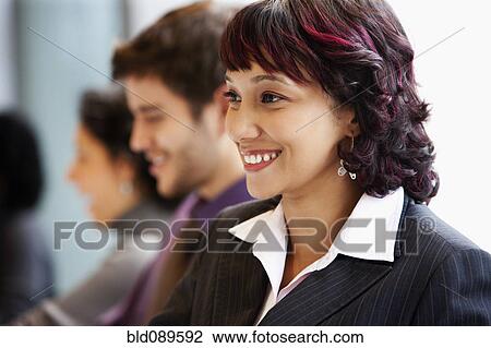 Stock Image - Smiling Hispanic businesswoman in office with co-workers. Fotosearch