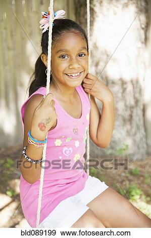 Stock Photo - Smiling Hispanic girl sitting on swing. Fotosearch