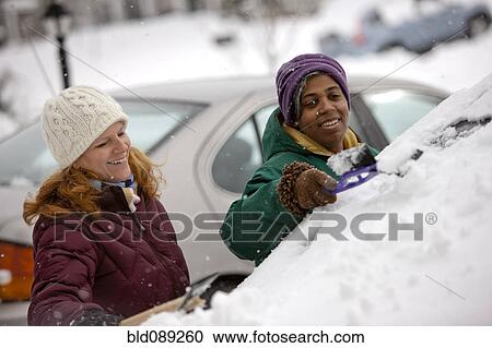 Stock Image - Two women scraping snow from windshield. Fotosearch
