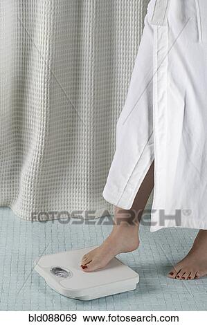 Stock Photo - Woman stepping onto bathroom scale. Fotosearch