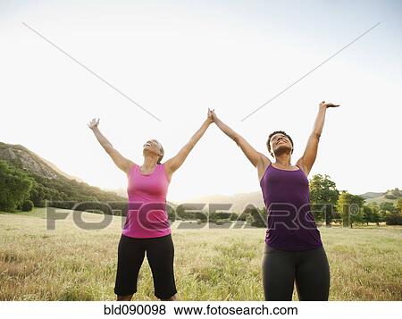 Stock Photo - Athletic women standing in field with arms raised. Fotosearch