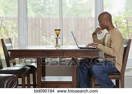 Picture - Black man using laptop at table. Fotosearch