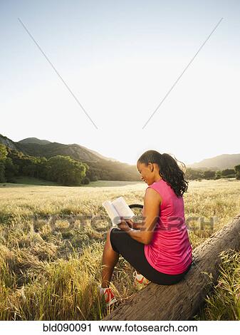 Stock Image - Black woman reading book in remote area. Fotosearch